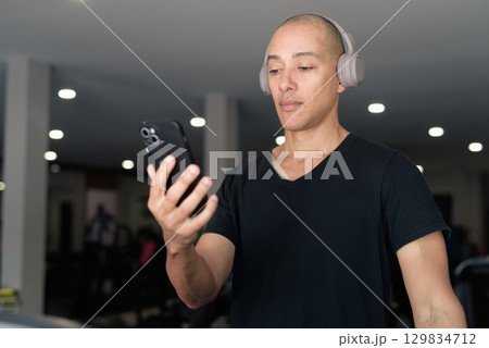 Hispanic bald man athlete in gym using mobile phone 129834712