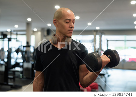 Hispanic bald man athlete in gym doing bicep curl with dumbbell 129834741