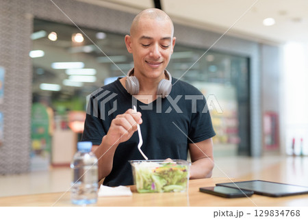 Man eating healthy salad in food court, health and wellness lifestyle Man eating healthy salad in food court, health and wellness lifestyle 129834768