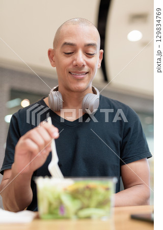 Man eating healthy salad in food court, health and wellness lifestyle Man eating healthy salad in food court, health and wellness lifestyle 129834769