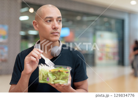 Man eating healthy salad in food court, health and wellness lifestyle 129834776