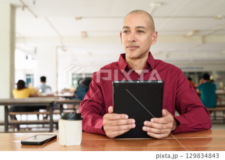 Man using digital tablet computer device at outdoor cafe restaurant table in urban academic setting Man using digital tablet computer device at outdoor cafe restaurant table in urban academic setting 129834843