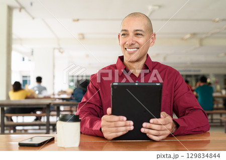 Man using digital tablet computer device at outdoor cafe restaurant table in urban academic setting Man using digital tablet computer device at outdoor cafe restaurant table in urban academic setting 129834844