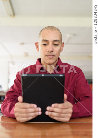 Man using digital tablet computer device at outdoor cafe restaurant table in urban academic setting 129834845