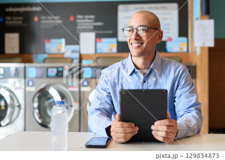 Man Using Tablet Computer While Sitting in Laundry Shop 129834873