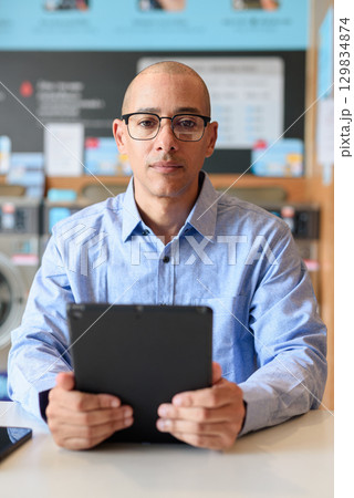 Man Using Tablet Computer While Sitting in Laundry Shop 129834874