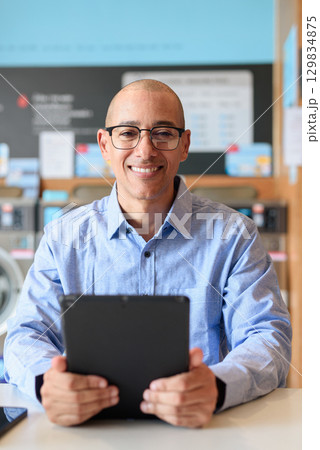 Man Using Tablet Computer While Sitting in Laundry Shop 129834875