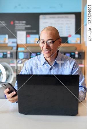 Businessman using laptop in laundry shop, focused and professional working concept 129834901