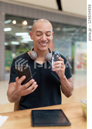 Man using tablet while eating salad and drinking water in mall cafe Man using tablet while eating salad and drinking water in mall cafe 129834956