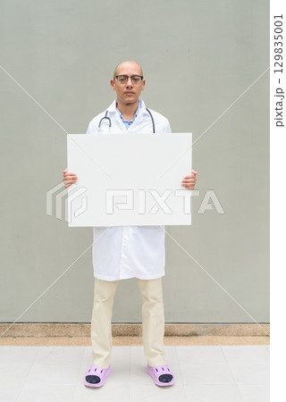 Full Length Portrait of Male Doctor in Lab Coat with Stethoscope Holding Placard with Copy Space 129835001