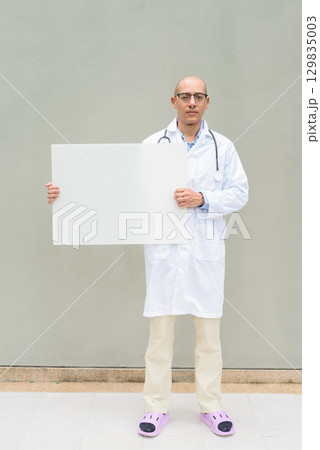 Full Length Portrait of Male Doctor in Lab Coat with Stethoscope Holding Placard with Copy Space 129835003