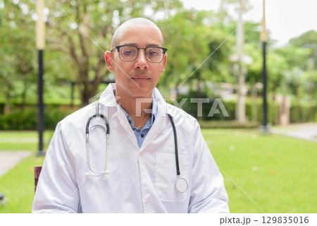 Doctor in uniform relaxing outdoors in hospital garden, smiling and confident looking at camera 129835016