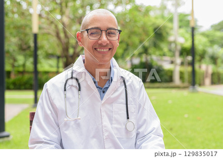 Doctor in uniform relaxing outdoors in hospital garden, smiling and confident looking at camera Doctor in uniform relaxing outdoors in hospital garden, smiling and confident looking at camera 129835017