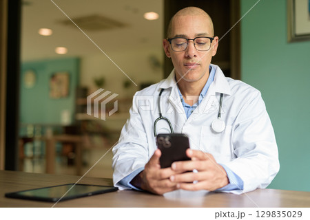 Doctor Sitting Indoors in Clinic or Hospital Area Library with Stethoscope Doctor Sitting Indoors in Clinic or Hospital Area Library with Stethoscope 129835029