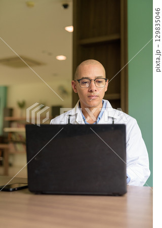 Doctor Sitting Indoors in Clinic or Hospital Area Library Using Laptop Computer 129835046