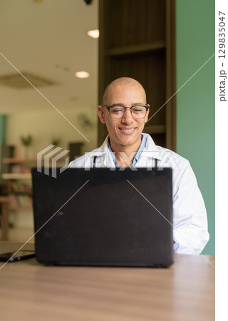 Doctor Sitting Indoors in Clinic or Hospital Area Library Using Laptop Computer 129835047