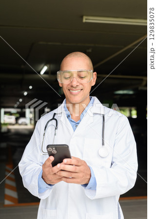 Bald Male Scientist Standing Outside Modern Research Facility Using Phone 129835078