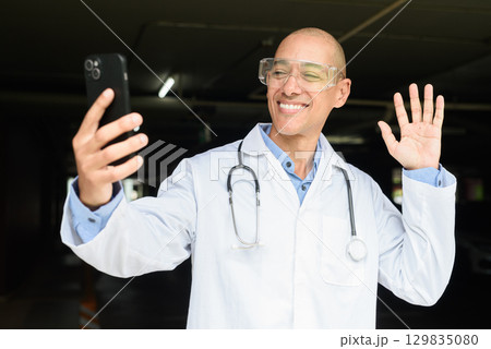 Bald Male Scientist Standing Outside Modern Research Facility Using Phone 129835080