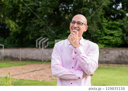 Bald Hispanic man thinking and looking up with hand on chin outdoors Bald Hispanic man thinking and looking up with hand on chin outdoors 129835138