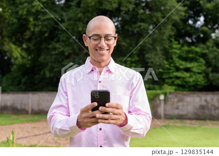 Bald Hispanic man wearing pink casual business shirt and eyeglasses outdoors 129835144