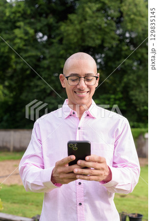 Bald Hispanic man wearing pink casual business shirt and eyeglasses outdoors 129835145