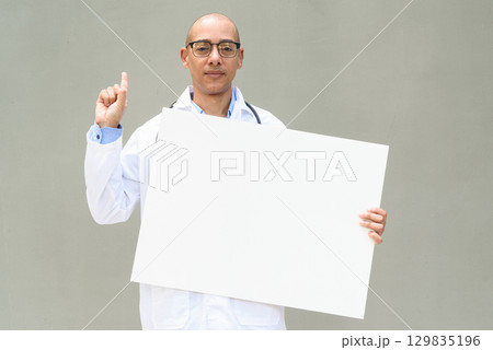 Hispanic Male Doctor in Lab Coat with Stethoscope on Plain Background Holding Empty Placard Hispanic Male Doctor in Lab Coat with Stethoscope on Plain Background Holding Empty Placard 129835196