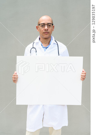Hispanic Male Doctor in Lab Coat with Stethoscope on Plain Background Holding Empty Placard Hispanic Male Doctor in Lab Coat with Stethoscope on Plain Background Holding Empty Placard 129835197