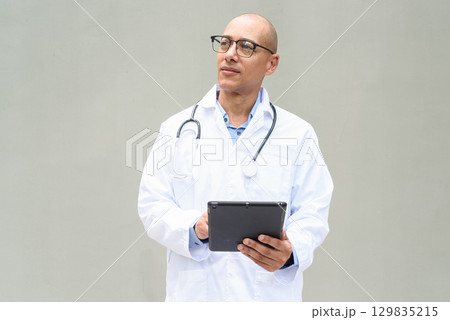 Hispanic Male Doctor in Lab Coat with Stethoscope on Plain Background Using Tablet Computer 129835215