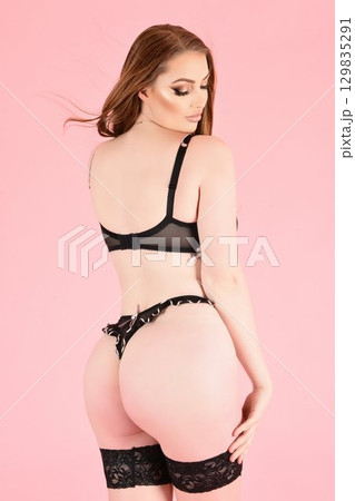 Beautiful redhead girl modelling provocative black lingerie, isolated against a pink background 129835291
