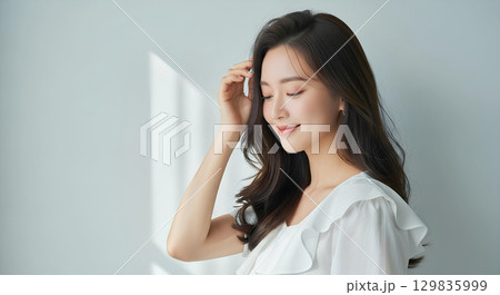 ロングヘアの白い服の若い女性が自然光の中で微笑むポートレート 129835999