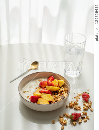 Granola or muesli with natural greek yogurt, strawberry and peach in a bowl on a white table Granola or muesli with natural greek yogurt, strawberry and peach in a bowl on a white table 129836433