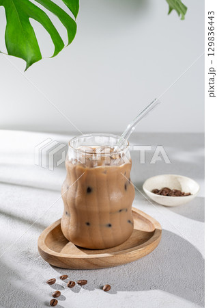 Ice latte coffee in a glass with milk and straw on a wooden plate on light background 129836443