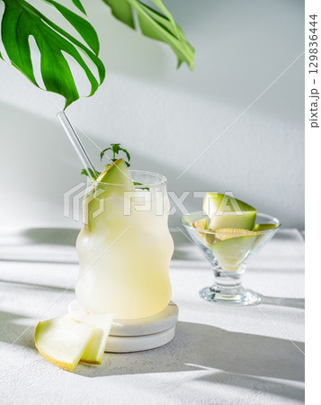 Cold lemonade or mojito in a glass with melon, straw and mint on a light background with pieces Cold lemonade or mojito in a glass with melon, straw and mint on a light background with pieces 129836444