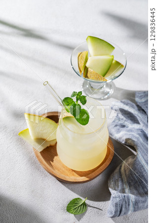 Refreshing lemonade or mojito in a glass with melon, straw and mint on a wooden plate Refreshing lemonade or mojito in a glass with melon, straw and mint on a wooden plate 129836445