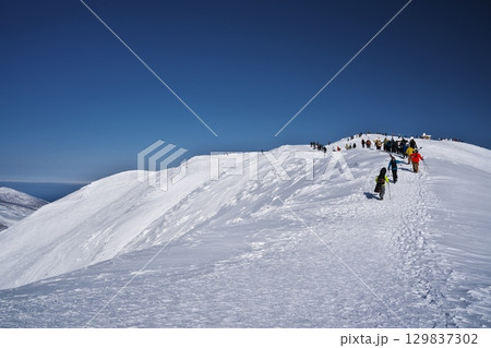 ニセコ東急 グラン・ヒラフ・ゲレンデからスキー場管理区域外をニセコアンヌプリへ登る人々 129837302