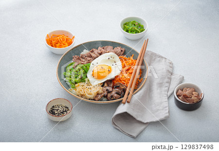 Traditional korean bibimbap with fried egg, beef and vegetables and other toppings on light background with chopsticks Traditional korean bibimbap with fried egg, beef and vegetables and other toppings on light background with chopsticks 129837498
