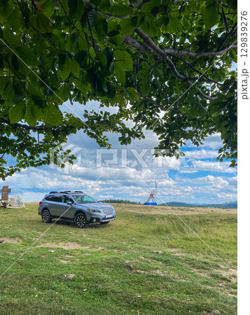 Silver SUV on Grassy Hill with Cloudy Sky Silver SUV on Grassy Hill with Cloudy Sky 129839276