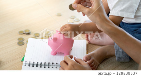 Family Finance. Child saving coins in piggy bank while parent takes notes. 129839337