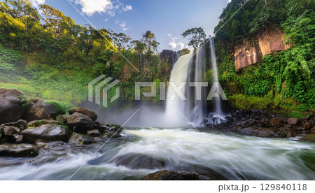 roaring waterfall crashing into rocks, surrounded by lush greenery 129840118