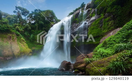 roaring waterfall crashing into rocks symbolizes power, surrounded by lush greenery 129840119