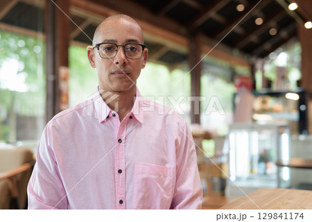 Bald Hispanic man wearing pink casual business shirt and eyeglasses in coffee shop cafe restaurant Bald Hispanic man wearing pink casual business shirt and eyeglasses in coffee shop cafe restaurant 129841174