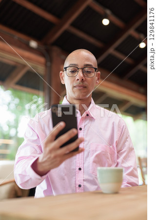 Bald Hispanic man wearing pink casual business shirt and eyeglasses in coffee shop cafe restaurant 129841176