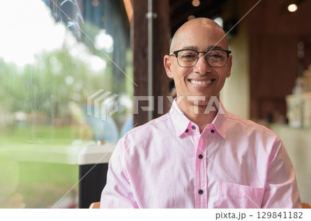 Happy bald Hispanic man wearing pink casual business shirt and eyeglasses in coffee shop cafe Happy bald Hispanic man wearing pink casual business shirt and eyeglasses in coffee shop cafe 129841182