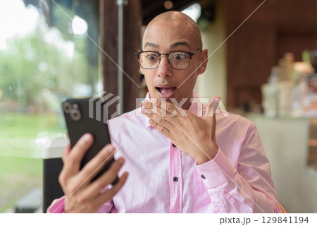 Shocked man using phone in coffee shop restaurant 129841194
