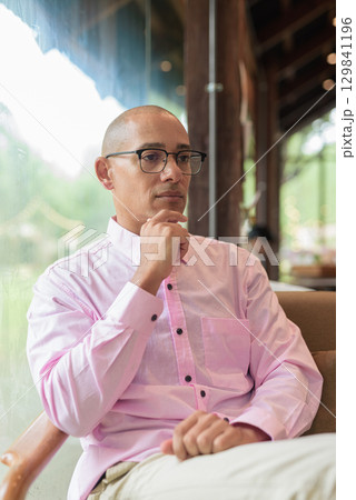 Bald Hispanic man wearing pink casual business shirt and eyeglasses in coffee shop cafe restaurant 129841196