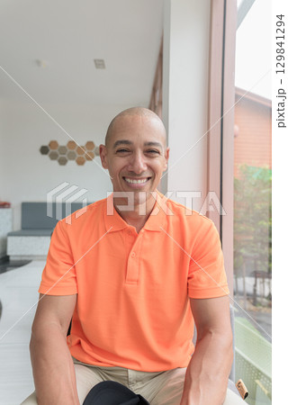 Bald Hispanic man face inside cafe restaurant wearing orange polo shirt smiling at camera Bald Hispanic man face inside cafe restaurant wearing orange polo shirt smiling at camera 129841294