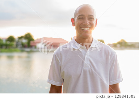 Summer portrait of bald man face headshot next to park lake during sunset with lens flare 129841305