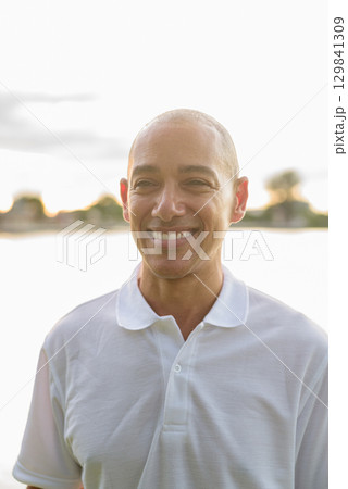 Summer portrait of bald man face headshot next to park lake during sunset with lens flare 129841309
