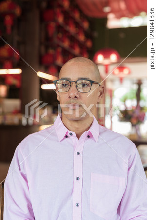 Bald Hispanic man wearing pink casual business shirt and eyeglasses in Chinese style tea house Bald Hispanic man wearing pink casual business shirt and eyeglasses in Chinese style tea house 129841336