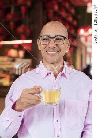 Bald Hispanic man wearing pink casual business shirt and eyeglasses in Chinese style tea house Bald Hispanic man wearing pink casual business shirt and eyeglasses in Chinese style tea house 129841347